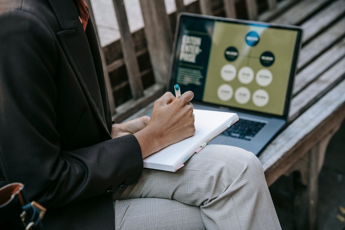 Web designer planning a project with a notebook and laptop outdoors, representing the discovery and strategy phase that good web designers invest in
